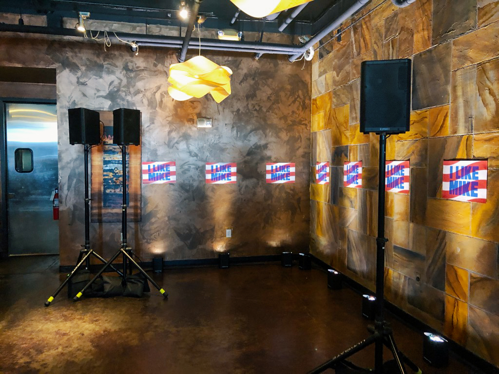 3 speakers on stands line the wall of a warm concrete room.