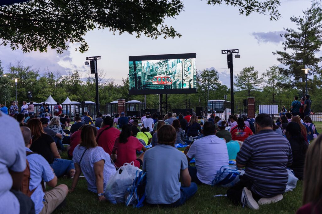 Hundreds of viewers watch a movie on a large screen outdoors
