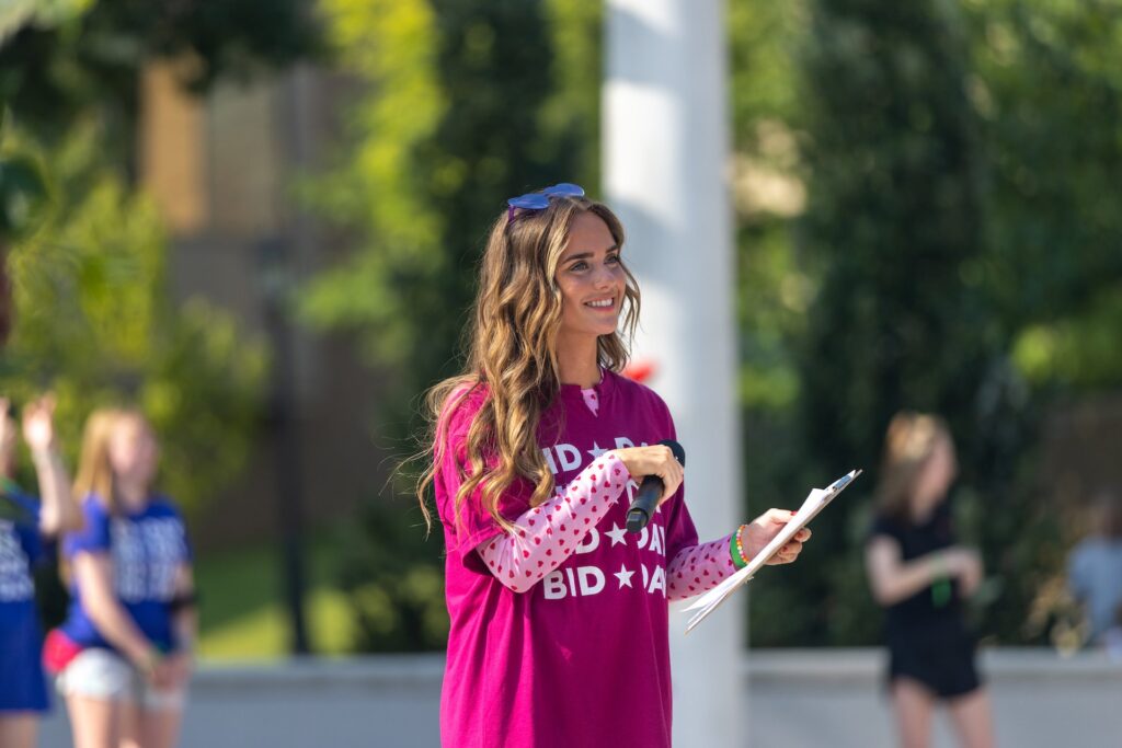 A young women speaks on stage about bid day and smiles