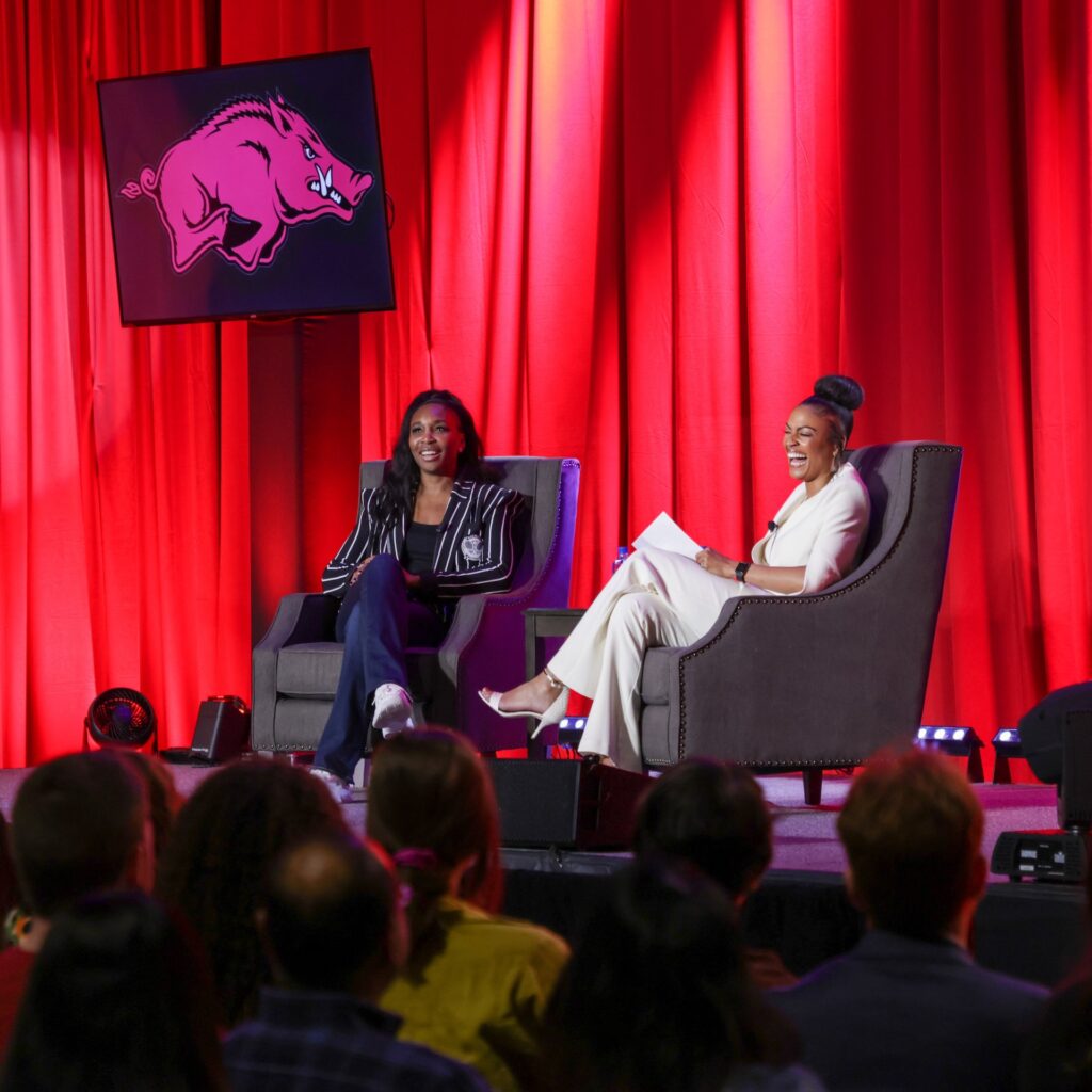 The athlete, Venus Williams, sits on stage and laughs with a presenter.