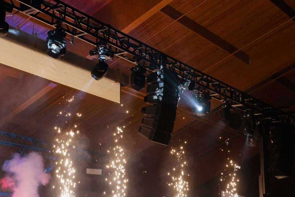 Lighting and speakers hang on truss above cold sparks.