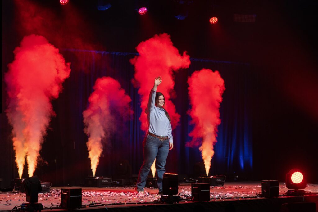 Youth member stands on stage with smoke filling the background.