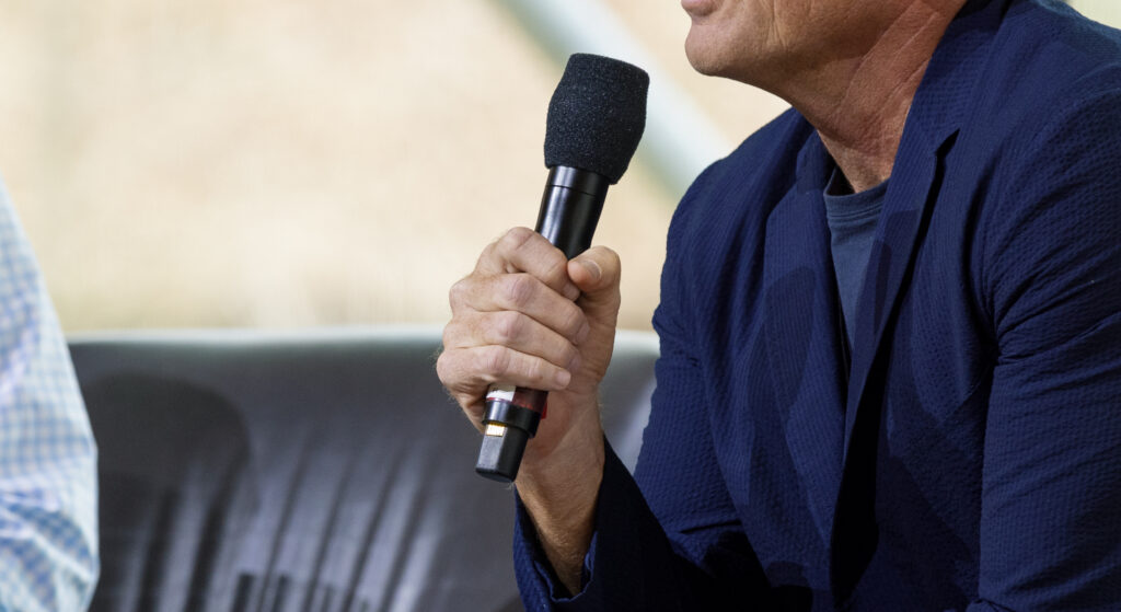 Presenter in a blue suit holds a wireless microphone. 