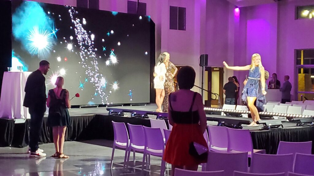 3 models walk down the catwalk in a purple room.